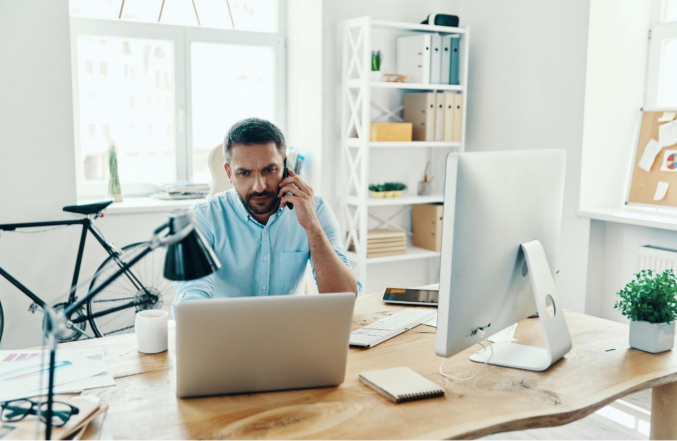 Man working at desk with computer and talking on mobile phone